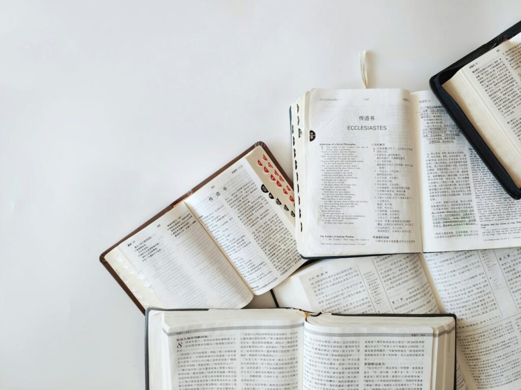 pexels-photo-22710978 Multiple Bibles open on a white background showing text from Ecclesiastes in different languages.